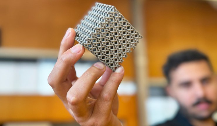 PhD candidate Jordan Noronha holding a sample of the new titanium lattice structure 3D printed in cube form. - RMIT University